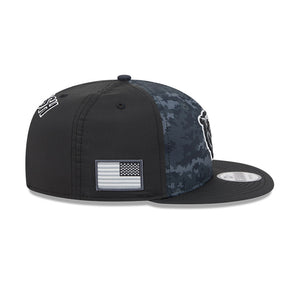 A New Era 9FIFTY snapback cap featuring a black front and brim, a digital camouflage pattern on the back panels, and a black-and-white American flag patch on the side.