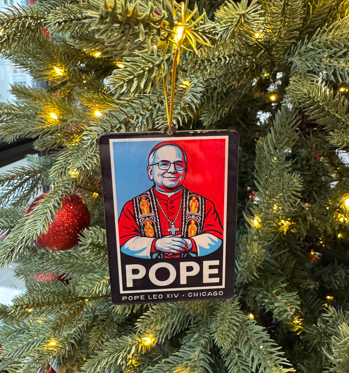 Christmas tree ornament with a depiction of Pope Leo XIV, hanging among green branches and lights.