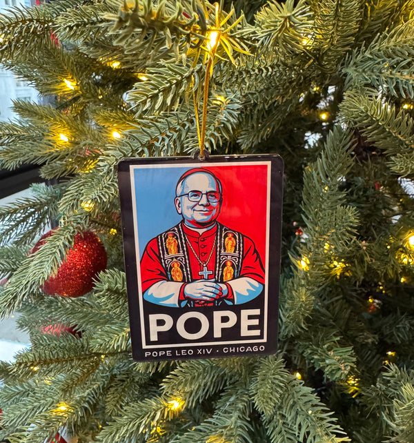 Christmas tree ornament with a depiction of Pope Leo XIV, hanging among green branches and lights.