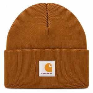 A classic ribbed knit beanie hat in a warm rust-orange color, featuring a white square Carhartt brand patch on the front cuff.