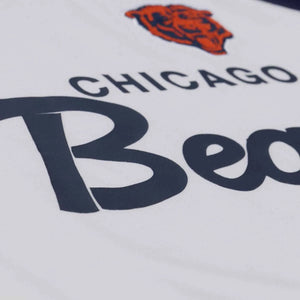 Close-up of a white Chicago Bears jersey or shirt fabric showing the navy team name, part of the orange bear head logo, and the word 'Bea' in navy script.
