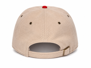 A beige canvas baseball cap shown from the back, featuring a small red button on top, metal ventilation eyelets, and an adjustable hook-and-loop strap closure.